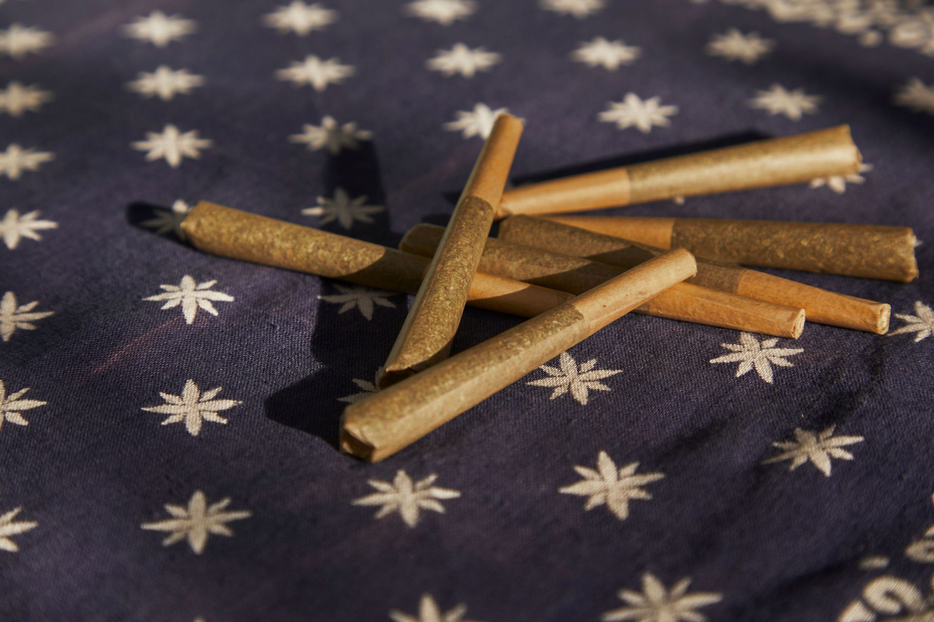 A collection of cannabis pre-rolled joints on a star-patterned blue fabric, captured indoors.